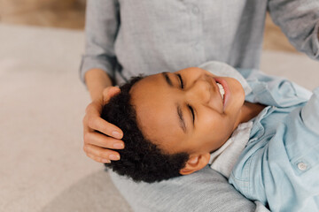 Boy resting at the knees of his caucasian mother while staying at home