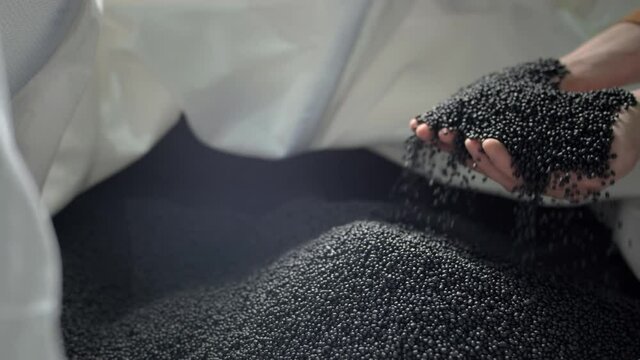 Hands lift polymer granules from a bag in a garbage recycling plant.