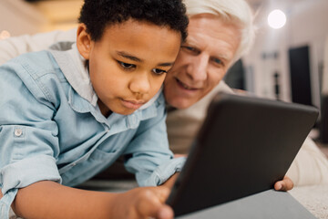 Father and son laying at the carpet with tablet and playing games at home