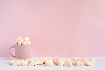 Pink mug full of marshmallows on a table across pink backround with copy space for text or image