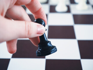 Hand holds chess pawn with a chess board background. Conceptual photo with selective focus and copy...