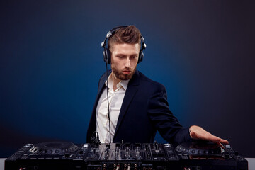 Man DJ in dark suit play music on a Dj's mixer. Studio shot. Dark blue background