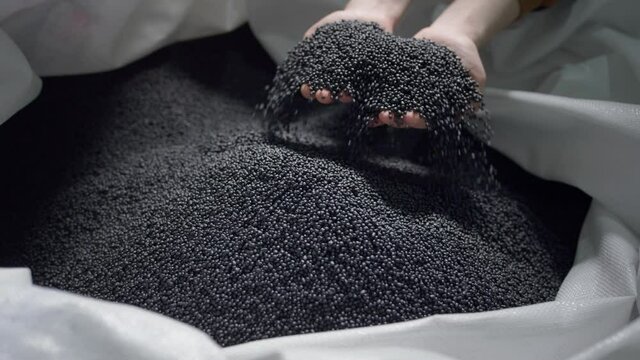 Hands lift polymer granules from a bag in a garbage recycling plant.