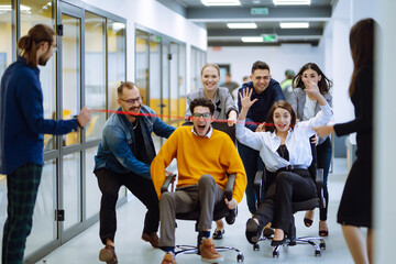 Friendly work team  ride chairs in office room cheerfully excited diverse employees laugh while...
