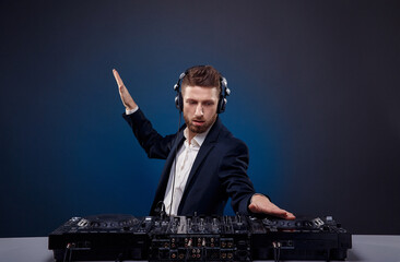 Man DJ in dark suit play music on a Dj's mixer. Studio shot. Dark blue background