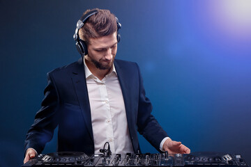 Man DJ in dark suit play music on a Dj's mixer. Studio shot. Dark blue background