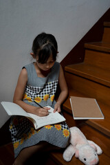 Fototapeta na wymiar Little girl writing book and having cookie at stairway at home.