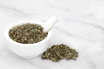 Coltsfoot herb leaves in a mortar with pestle used in herbal medicine to treat inflammation, asthma, gout, arthritis and coughs. On marble background. Asteraceae.