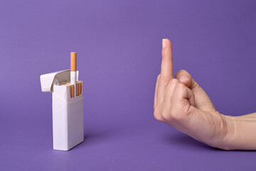 A hand giving the middle finger to a cigarette treat from a pack. Refusing cigarette. Stop smoking...