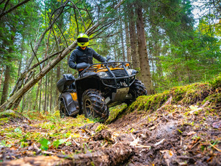ATV with driver front view. He drives off-road in the forest. Offroad travel adventure trip expedition. Extreme recreation activity on an ATV. Travel on a yellow ATV. Man posing on a quad bike