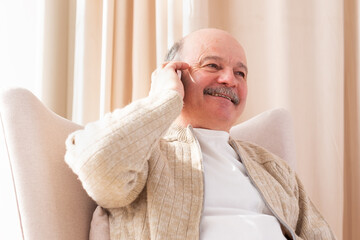 Senior man talking on mobile phone with his family sitting at the living room.