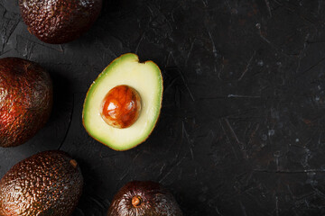 Ripe sliced Hass Avocado with a bone on a black textured background.