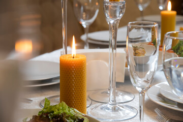 Romantic candlelight dinner in a beautiful restaurant. Natural wax candles on the table. Lighted candles. Side view on the served banquet restaurant table with candles, wine glasses, napkins, plates.