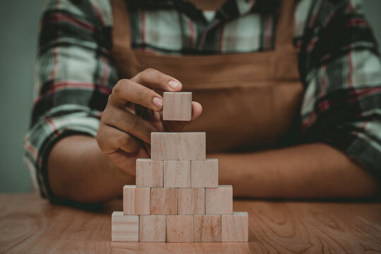 Hands of carpenter putting wood cube block and arrang on top of pyramid,business concept for growth success process.