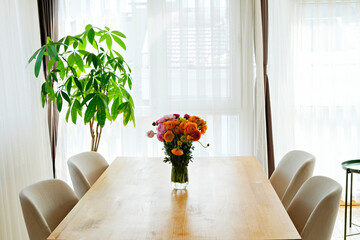 Close up shot of wooden dining table with beautiful ranunculuses in glass vase. A bouquet of mixed persian buttercup flowers in soft natural light from a window. Copy space, close up, background.
