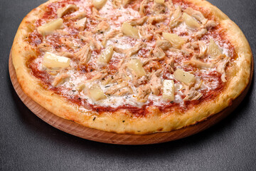 Tasty fresh oven pizza with tomatoes, cheese and pineapple on a dark concrete background
