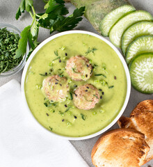 Soup puree of green radish and potatoes, parsley with meatballs, croutons in a bowl on a light gray background top view