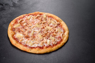 Tasty fresh oven pizza with tomatoes, cheese and pineapple on a dark concrete background