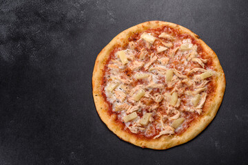 Tasty fresh oven pizza with tomatoes, cheese and pineapple on a dark concrete background