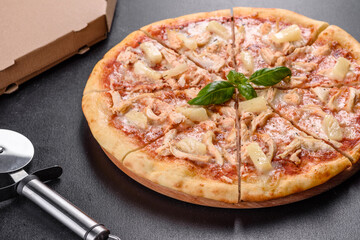 Tasty fresh oven pizza with tomatoes, cheese and pineapple on a dark concrete background
