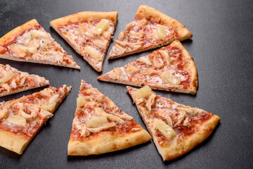 Tasty fresh oven pizza with tomatoes, cheese and pineapple on a dark concrete background