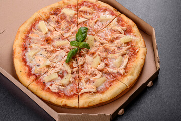 Tasty fresh oven pizza with tomatoes, cheese and pineapple on a dark concrete background