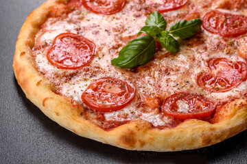 Tasty fresh oven pizza with tomatoes, cheese and basil on a concrete background