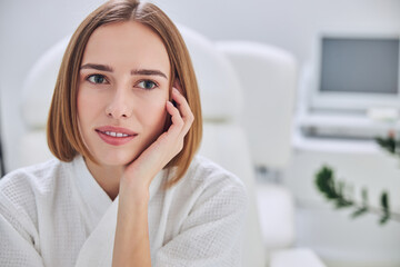 Young attractive redheaded female holding her hand near head while posing at the photo camera in spa relax complex