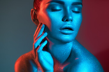 Fashion model woman in colorful bright sparkles and neon lights posing in studio, on black,...