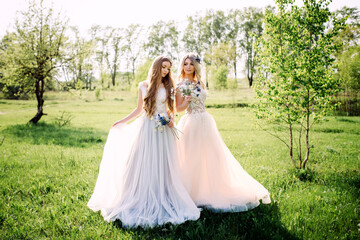 Two beautiful bridesmaids in white wedding dresses with bouquet on a sunny day in a summer nature