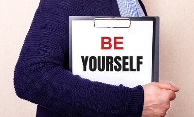 BE YOURSELF is written on a white sheet held by a man standing sideways