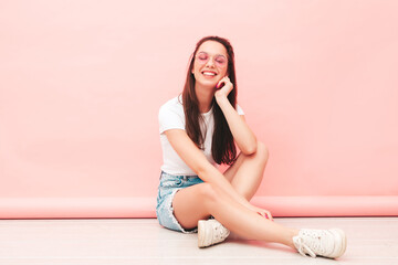 Young beautiful smiling female in trendy summer hipster clothes. Sexy carefree woman posing near pink wall in studio. Positive model having fun indoors. Cheerful and happy