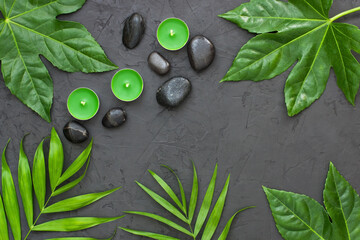 Spa concept - candles, stones and green leaf on dark surface, flat lay