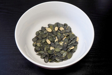 in a beige round plate are green-colored roasted pumpkin seeds. side view . cooking at home