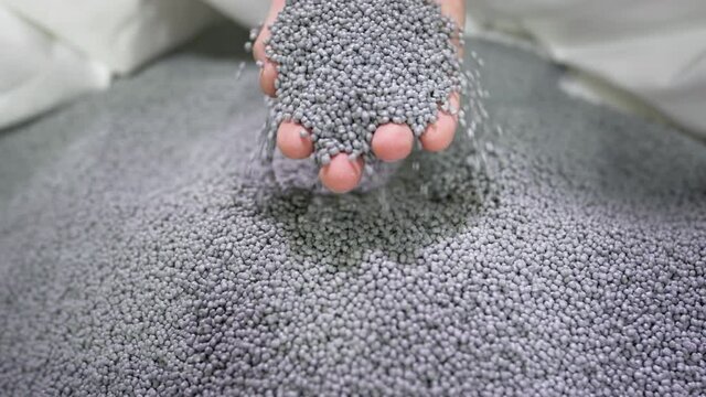 Hands lift polymer granules from a bag in a garbage recycling plant.