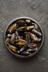Fresh and raw sea mussels in black ceramic bowl placed on dark stone background