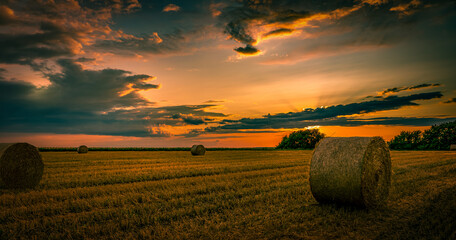 A bright orange sunset over a mown field of wheat where straw bales were left lying