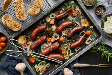 Top view on delicious grilled sausages served with onion, tomatoes, garlic, bread and herbs