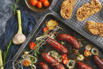 Tasty grilled homemade rosemary sausages placed on iron frying tray over rustic dark stone table