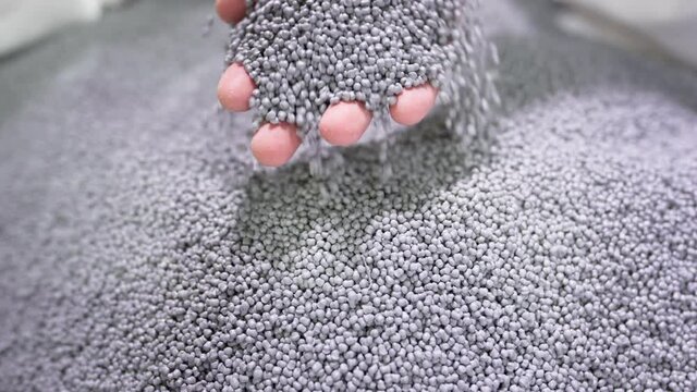 Hands lift polymer granules from a bag in a garbage recycling plant.