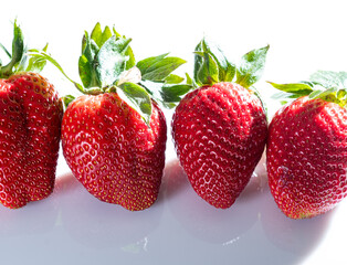 Four very red strawberries with their green leaves on a white background.