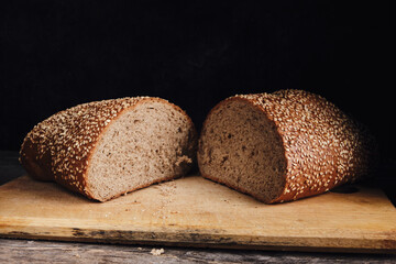 Two halves of sliced bread sprinkled with sesame seeds on a wooden cutting board.