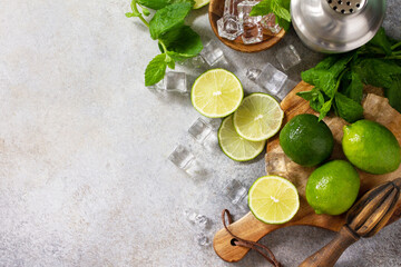 Refreshing cold summer Mojito cocktail making. Mint, lime, ice ingredients and bar utensils on a stone or concrete table. Top view flat lay. Copy space.