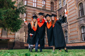 Graduates embrace, enjoy and look at the camera on the graduation ceremony.