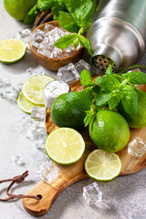 Refreshing cold summer Mojito cocktail making. Mint, lime, ice ingredients and bar utensils on a stone or concrete table.