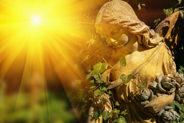 Antique statue of angel with sad expression that looks up in the sunlight.