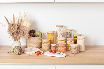 Assortment of grains, cereals and pasta in glass jars and vegetables on wooden table