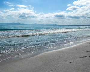 Dia soleado con alguna nuble con el mar cristalino y pequeñas olas con montañas en el horizonte