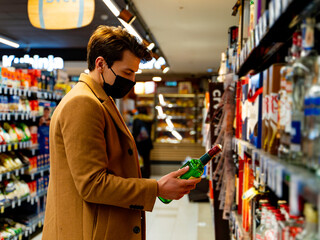handsome man wearing a protective mask during the covid-19 in the supermarket taking groceries on the shelf