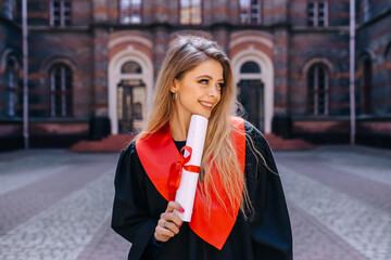 Fototapeta premium A young girl with long hair, a graduate holding a diploma on the background of the university.